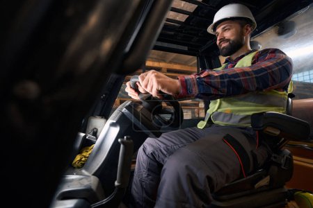 Téléchargez les photos : Man in protective clothes and helmet sitting in the loading machine and driving - en image libre de droit