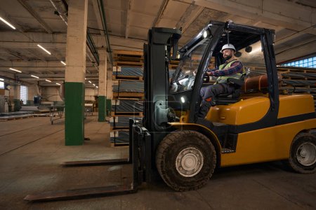 Téléchargez les photos : Male in protective clothes and helmet sitting in the loading machine and driving in workshop - en image libre de droit