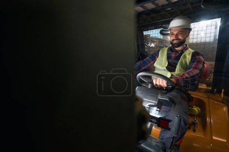 Foto de Male in protective clothes and helmet sitting in the loading machine and driving - Imagen libre de derechos