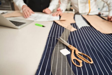 Téléchargez les photos : Cropped photo of two tailors standing at cutting table with paper patterns and sewing tools - en image libre de droit
