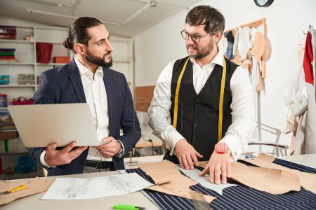 Photo for Couturier laying out pattern pieces on cloth in presence of his colleague - Royalty Free Image