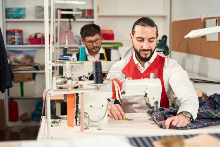 Téléchargez les photos : Focused tailor and his serious colleague overcasting fabric on overlockers in atelier - en image libre de droit