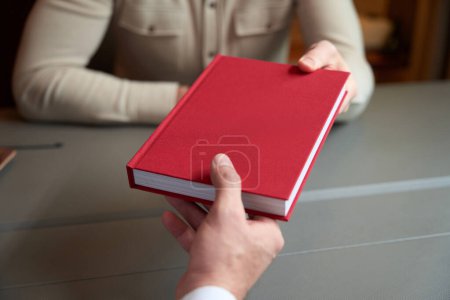 Photo for Man gives a red book to a colleague, the men are sitting at the table - Royalty Free Image