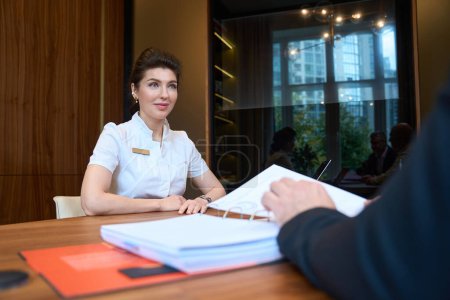 Téléchargez les photos : Charming female doctor and clinic client communicate in a stylish office, a folder with working material is on the table - en image libre de droit