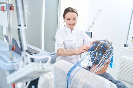 Photo for Woman diagnostician attaches sensors to the patient head, she performs an EEG - electroencephalography procedure - Royalty Free Image