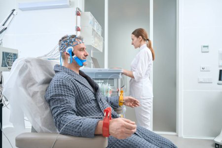 Foto de Modern EEG procedure - electroencephalography in a medical center, a patient in a hospital gown is connected to special equipment - Imagen libre de derechos