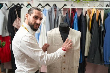 Téléchargez les photos : Smiling contented Caucasian tailor fitting customer waistcoat on dummy in his workshop - en image libre de droit