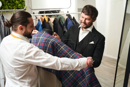 Foto de Smiling customer selecting material for his new suit aided by experienced tailor - Imagen libre de derechos