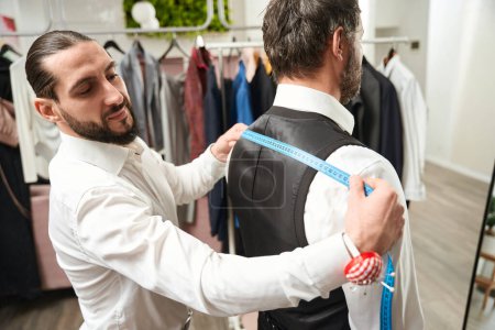 Photo for Smiling pleased clothier measuring shoulder width of adult man using tape measure - Royalty Free Image