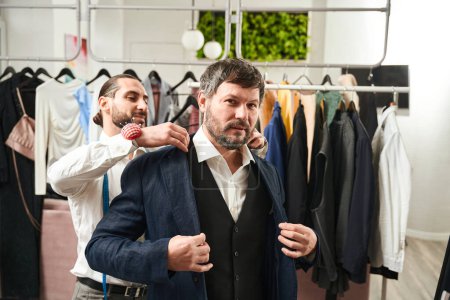 Téléchargez les photos : Client trying on new item of clothing assisted by his personal tailor - en image libre de droit