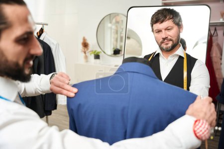 Téléchargez les photos : Professional tailor trying on client jacket on mannequin in presence of his colleague - en image libre de droit