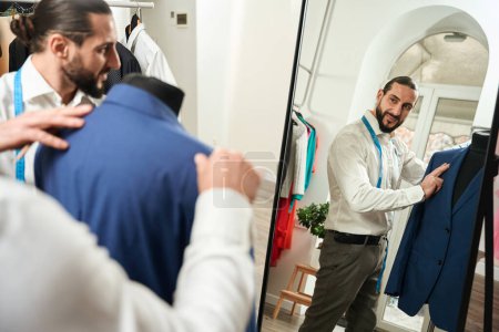 Téléchargez les photos : Focused professional tailor trying on jacket on mannequin assisted by his colleague - en image libre de droit