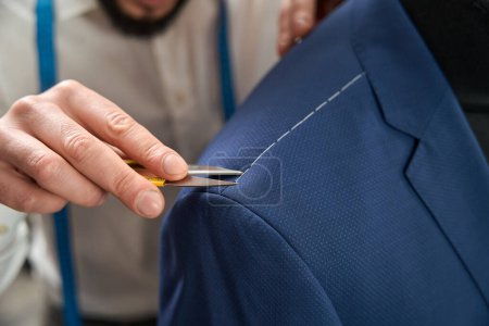 Foto de Cropped photo of clothier pulling out thread from suit jacket shoulder using sharp tool - Imagen libre de derechos