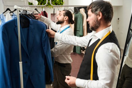 Téléchargez les photos : Side view of stylist and his colleague looking at garments on clothing rack - en image libre de droit