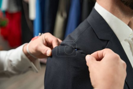 Téléchargez les photos : Close-up of clothier hands pinning sleeve to jacket armhole on male client - en image libre de droit