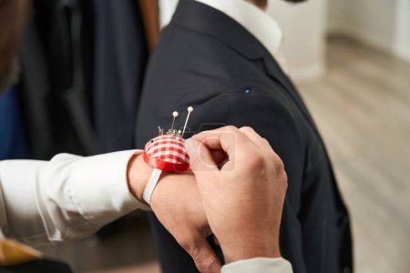 Téléchargez les photos : Cropped photo of clothier pulling pin from wrist-held pincushion in front of client - en image libre de droit