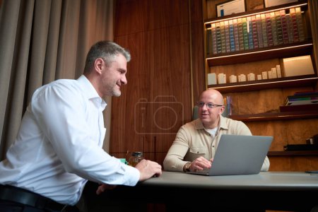 Foto de Waist up portrait of two confident males while they using laptop during the successful negotiation in the bright office - Imagen libre de derechos
