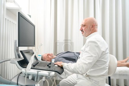 Photo for Waist up side view portrait of handsome seriously doctor is doing ultrasound examining of patient health in the medical center - Royalty Free Image