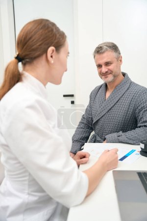Foto de Cintura arriba vista frontal retrato del guapo hombre caucásico está hablando con la doctora en la oficina de medicina - Imagen libre de derechos