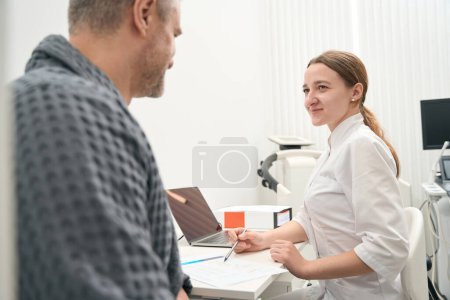 Photo for Side view portrait of smiling elegant female doctor is talking with patient in his medicine office - Royalty Free Image