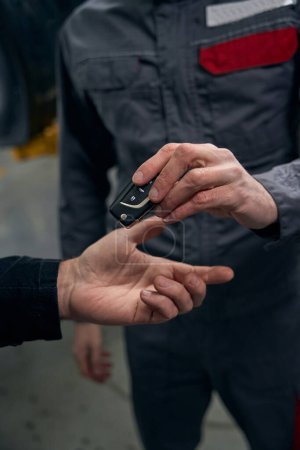 Photo for Mechanic in protective clothes standing in tire fitting, holding car keys and giving it to client - Royalty Free Image