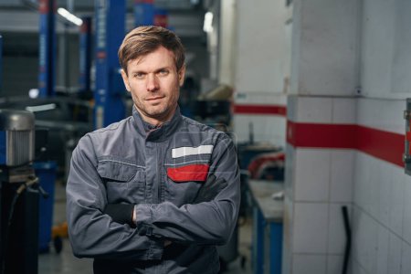 Téléchargez les photos : Portrait of mechanic in protective clothes standing in tire fitting and looking at the camera - en image libre de droit