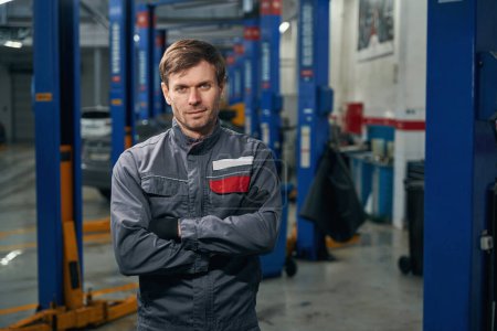 Photo for Portrait of male in protective clothes standing in tire fitting and looking at the camera - Royalty Free Image