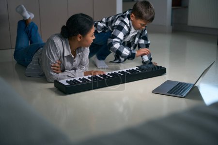 Photo for Mom helps son with online learning to play the digital piano, they have a great time together - Royalty Free Image