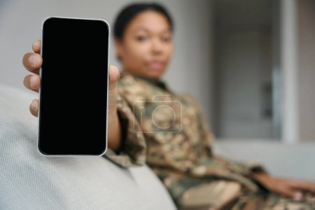 Foto de African american female soldier demonstrates the screen of the phone, she is in military clothes - Imagen libre de derechos