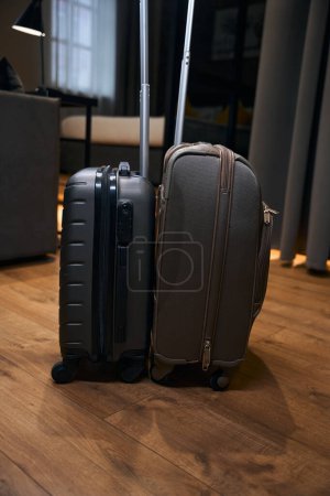 Téléchargez les photos : Deux sacs sombres de voyage sur roues avec poignées avec des choses sont dans l'appartement, préparé pour le voyage - en image libre de droit