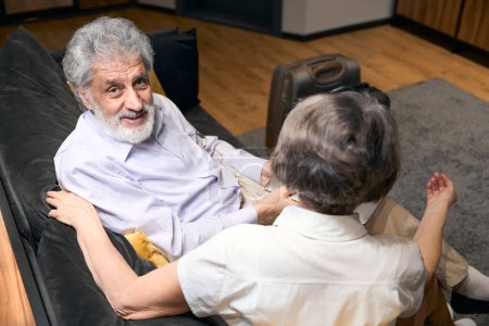 Photo for Elderly male and woman sitting on sofa in hotel, talking and looking at the camera - Royalty Free Image