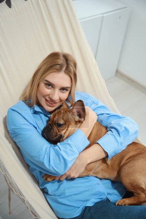 Téléchargez les photos : Souriant heureux maître animal de compagnie couché avec son bouledogue français préféré dans hamac - en image libre de droit