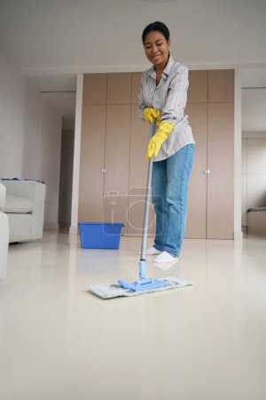Photo for Female african american mopping floor in living room, woman in comfortable casual clothes - Royalty Free Image