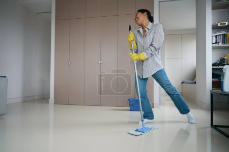 Téléchargez les photos : Woman started a cheerful cleaning in the living room, she sings and dances while washing the floor - en image libre de droit
