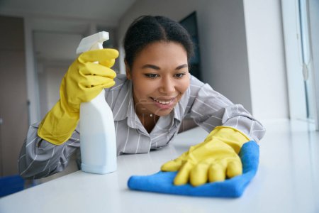 Foto de Superficie de limpieza femenina afroamericana feliz con trapo, mujer que trabaja en ropa casual - Imagen libre de derechos