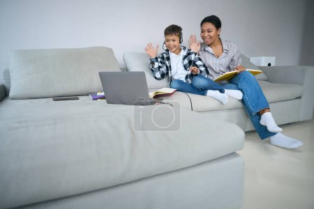 Téléchargez les photos : Online learning at home, a boy and his mom are sitting on the couch with a laptop, headset, books - en image libre de droit