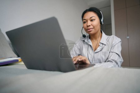 Foto de Estudiante de cursos de vídeo trabaja en una computadora en una habitación luminosa, una mujer tiene un auricular de computadora - Imagen libre de derechos