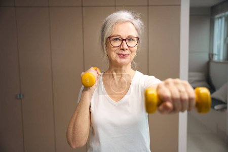 Téléchargez les photos : Energetic pensioner goes in for sports with dumbbells, she is cute and cheerful - en image libre de droit