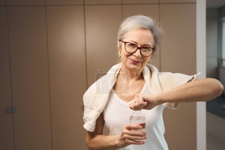 Téléchargez les photos : La grand-mère aux cheveux gris ouvre une bouteille d'eau, une femme a une serviette sur les épaules - en image libre de droit