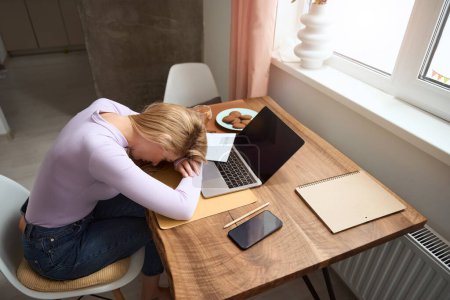 Photo for Exhausted modern young businesswoman lying in front of laptop screen on table - Royalty Free Image