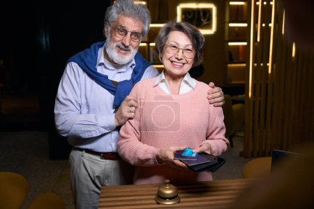 Photo for Joyful pensioners stand at the reception desk with passports, they are in travel clothes - Royalty Free Image