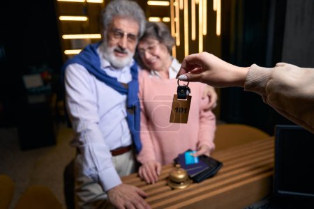 Photo for Cute grandparents receive the keys to the hotel room at the reception desk, the lady of the passport - Royalty Free Image