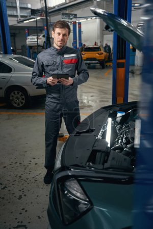 Foto de Hombre con ropa protectora de pie en el montaje de neumáticos y la celebración de la computadora portátil, mirando a la cámara - Imagen libre de derechos