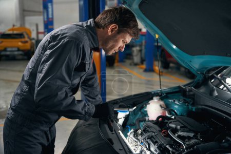 Foto de Hombre en ropa protectora de pie en el montaje de neumáticos y el motor de inspección de fugas de aceite - Imagen libre de derechos