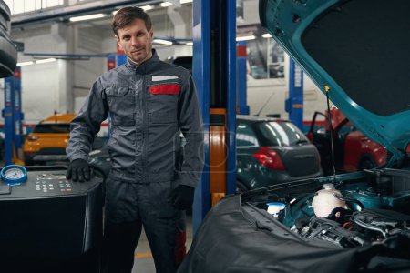 Téléchargez les photos : Homme en vêtements de protection debout dans le montage de pneus près du dispositif de ravitaillement en carburant climatiseur de voiture - en image libre de droit