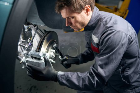 Photo for Man in protective clothes standing in tire fitting near car and checking caliper - Royalty Free Image