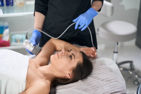 Photo for Woman lying on couch in salon, cosmetologist in protective gloves doing RF lifting for arm - Royalty Free Image