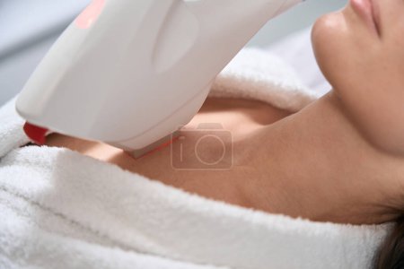 Téléchargez les photos : Jeune femme couchée sur le canapé dans le salon, médecin dans des gants de protection faisant IPL photorejuvenation pour le corps - en image libre de droit