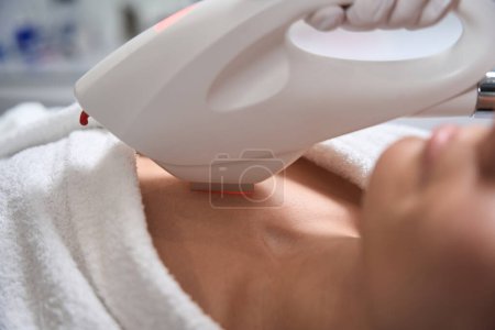 Photo for Young lady lying on couch in salon, medic in protective gloves doing IPL photorejuvenation for body - Royalty Free Image
