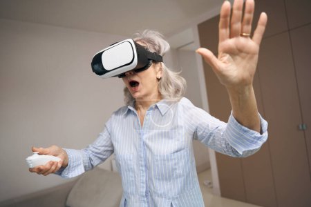 Foto de Entusiasta mujer mayor está jugando un juego virtual, ella está utilizando gafas de realidad virtual - Imagen libre de derechos